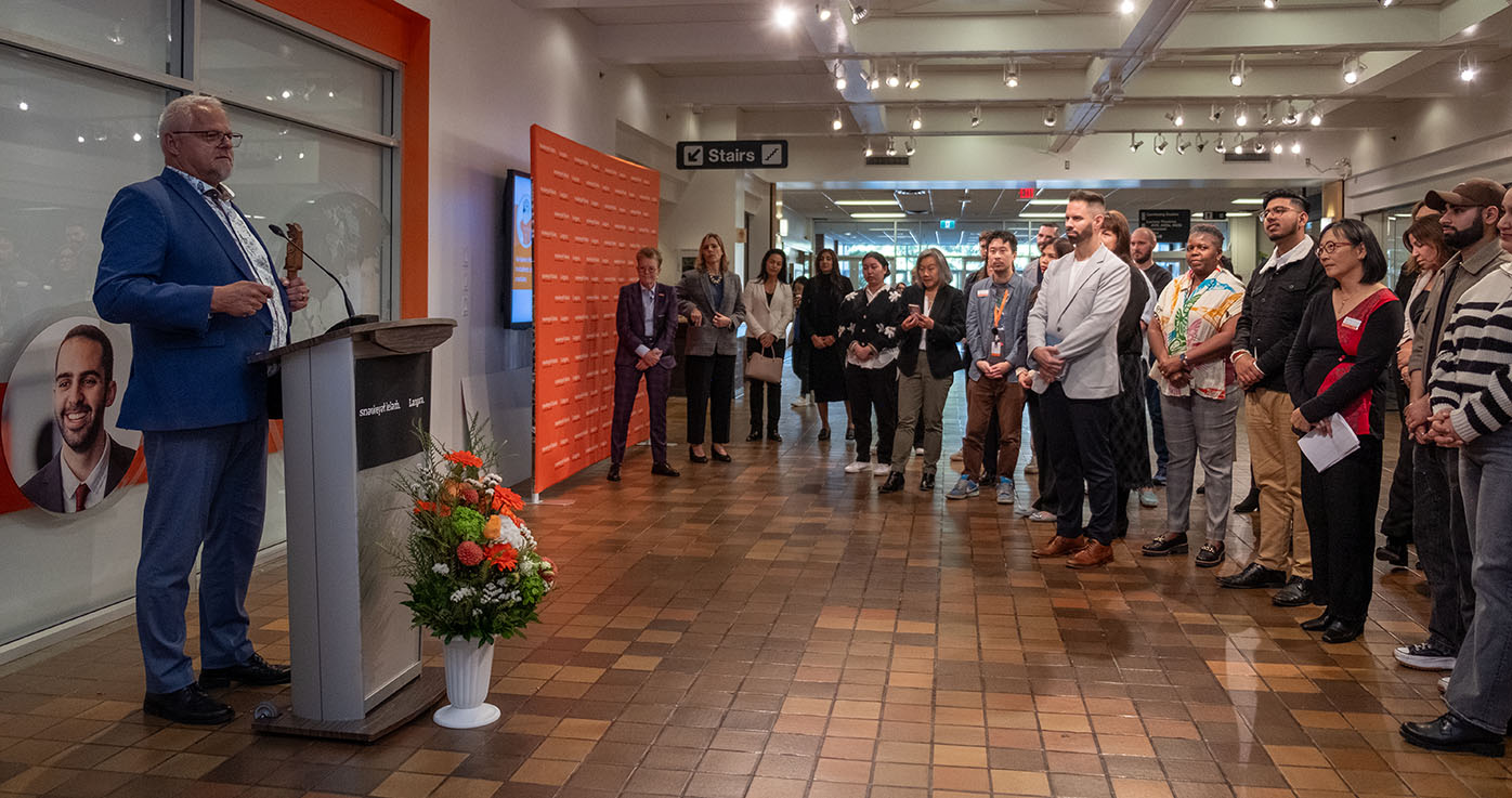 Clark Hortsing speaks to a crowd from a podium in the Langara A-building while wearing a blue suit.