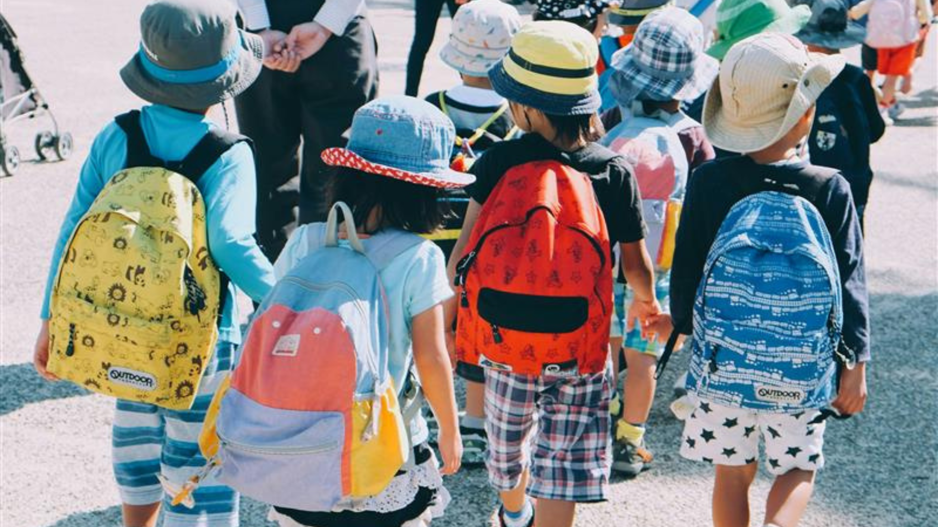 Four children in backpacks walking on concrete.