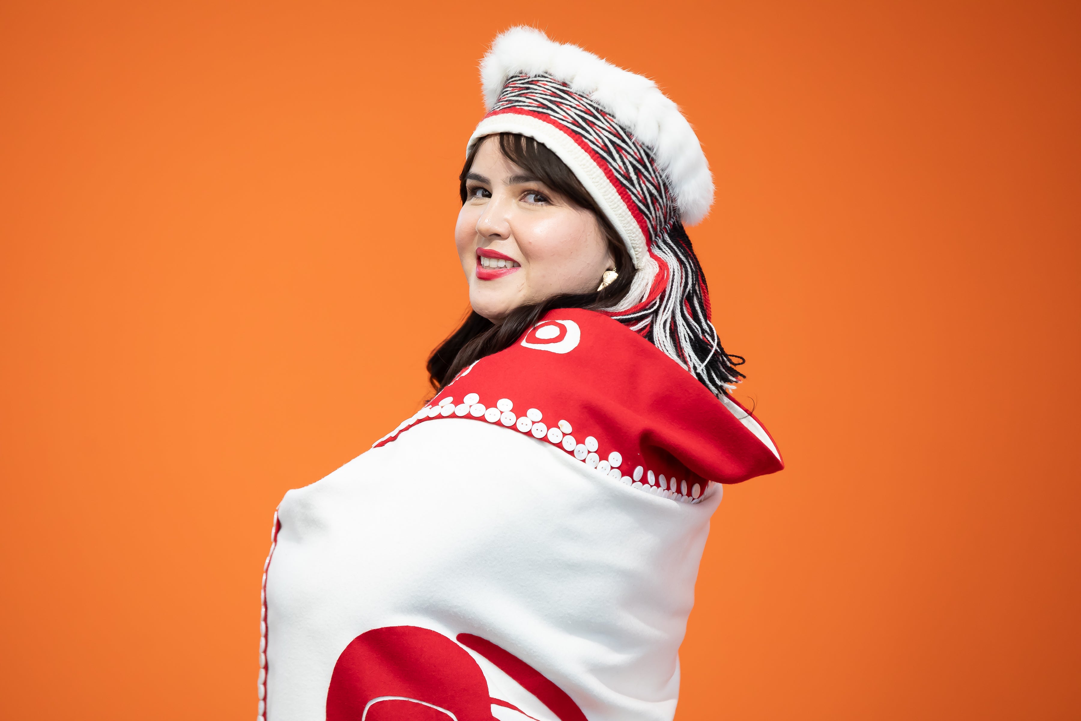 Nursing graduate, Cecelia Simeon, wearing traditional Haida garments against an orange background.