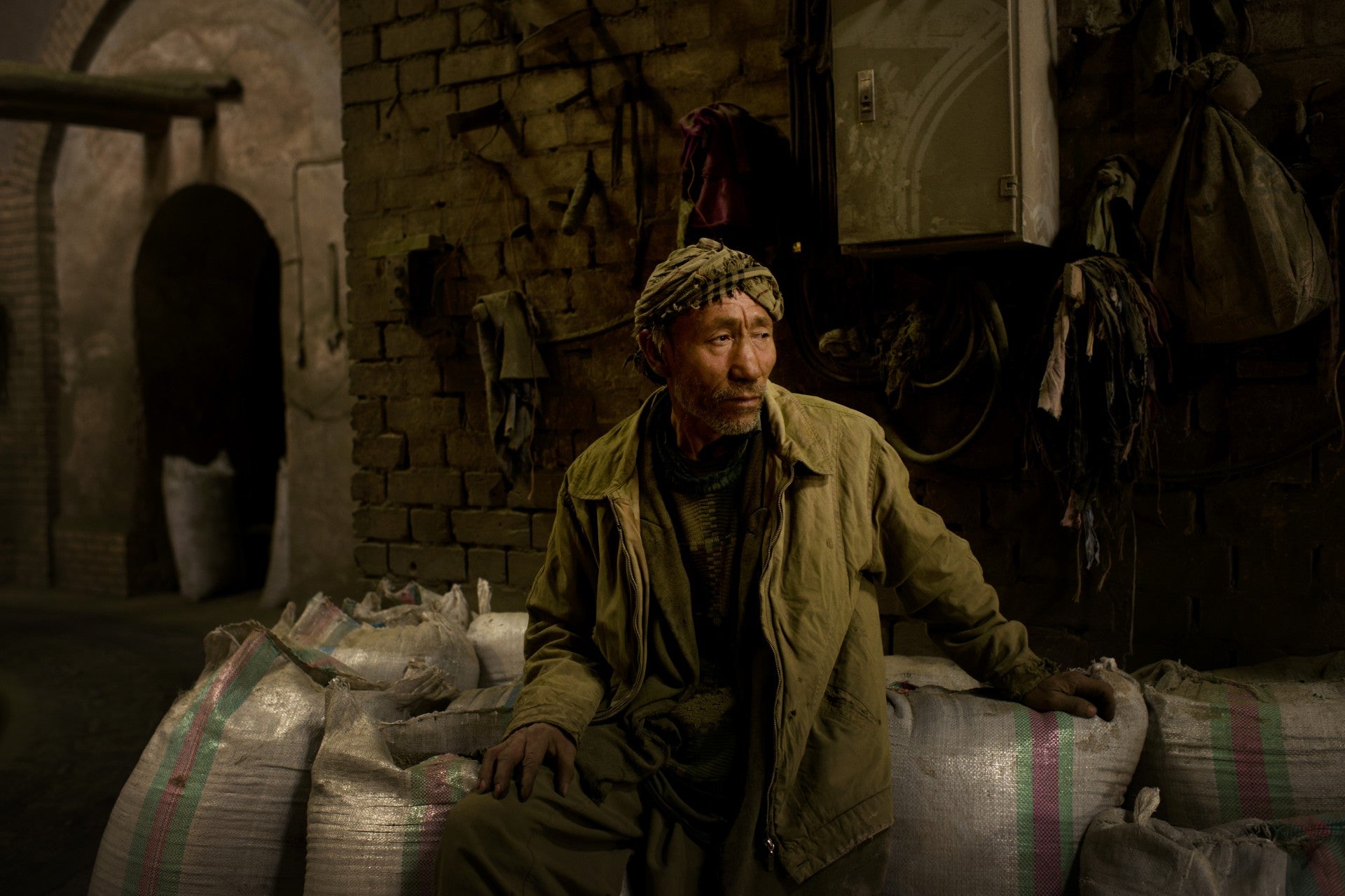 A lone man sits pensively on a pile of bags.