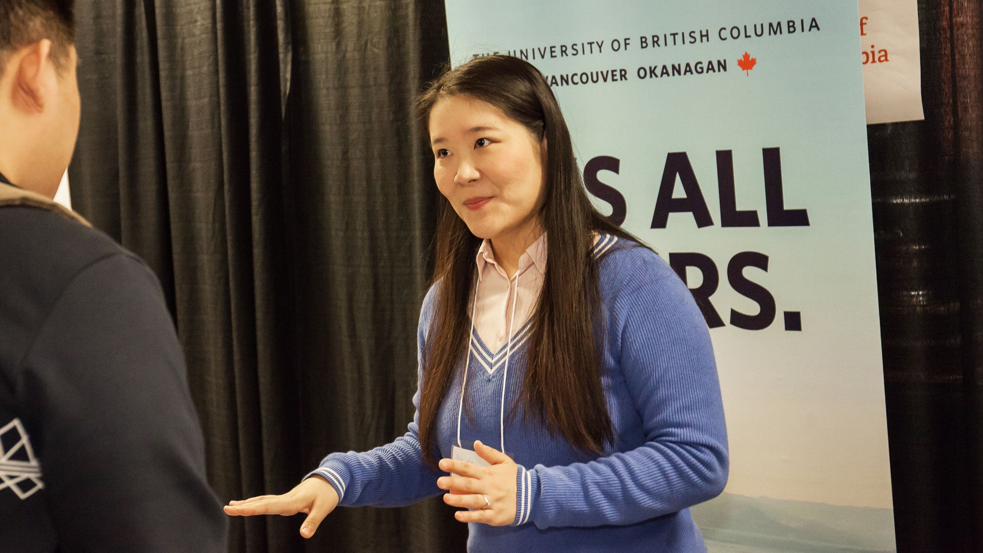 A woman in a blue sweater advises a student on transfer options to the University of British Columbia Okanagan at a Langara University Fair.