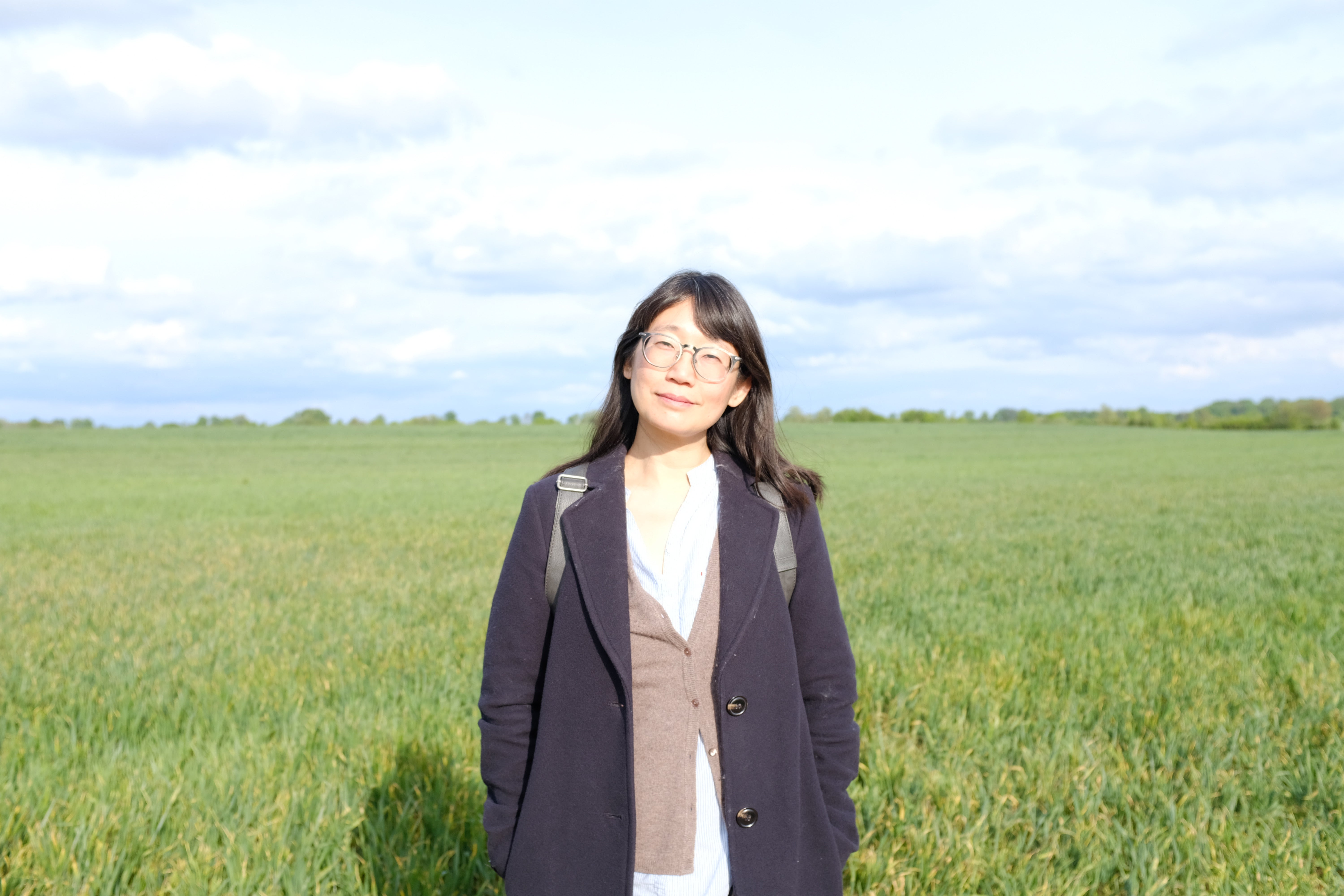 2026 Writer in Residence, Madeleine Thien, stands in a grassy field. Photo by Rawi Hage.