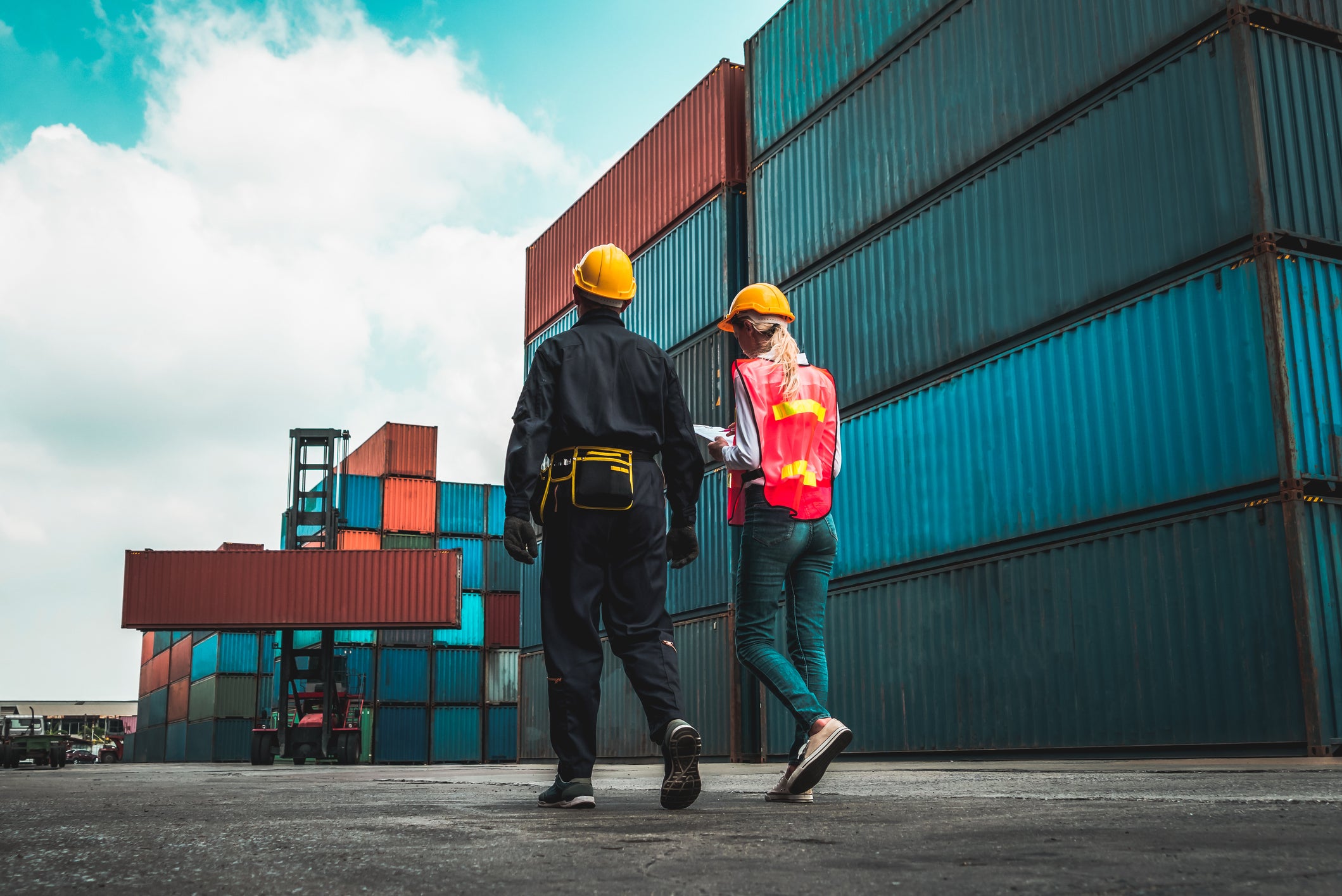Two supply chain and logistics workers walking amongst shipping containers.