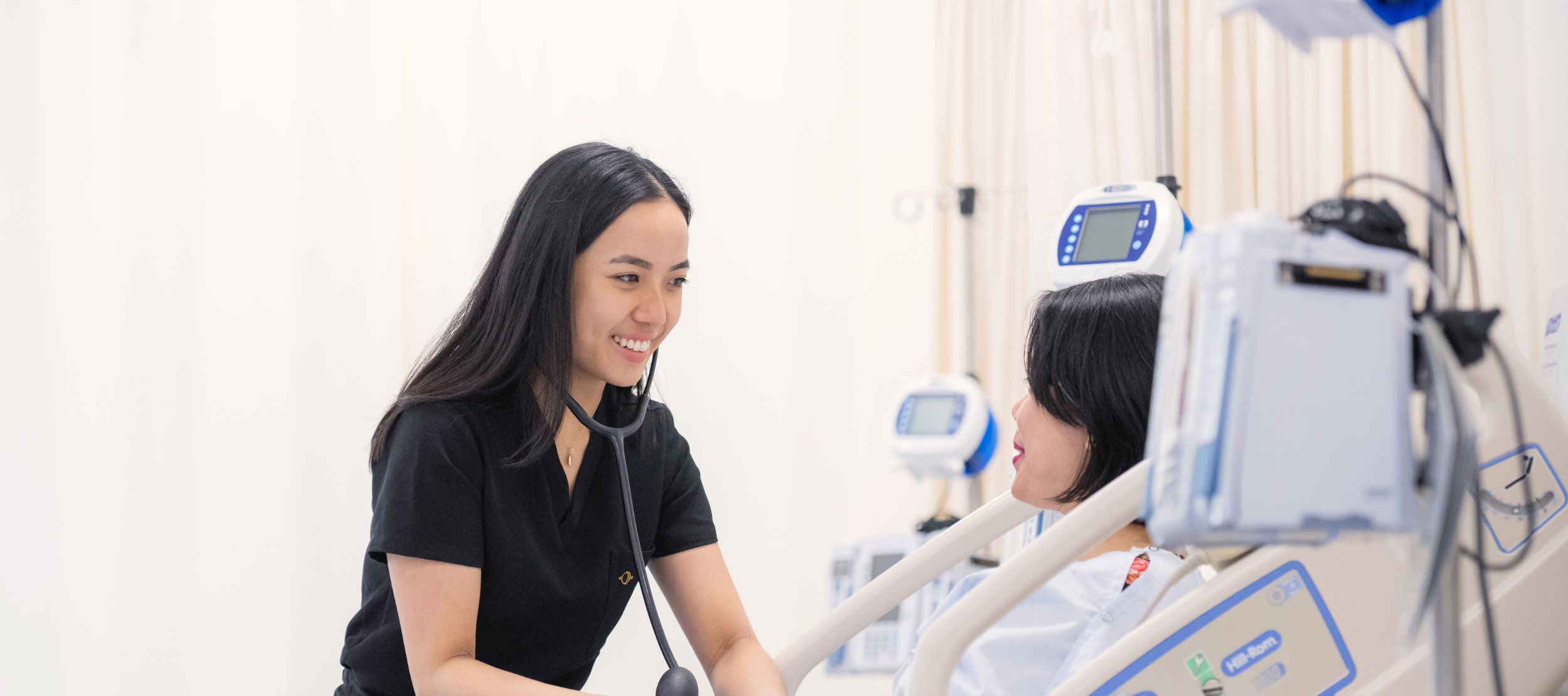 A nurse with a stethoscope providing care to a patient in a hospital bed.