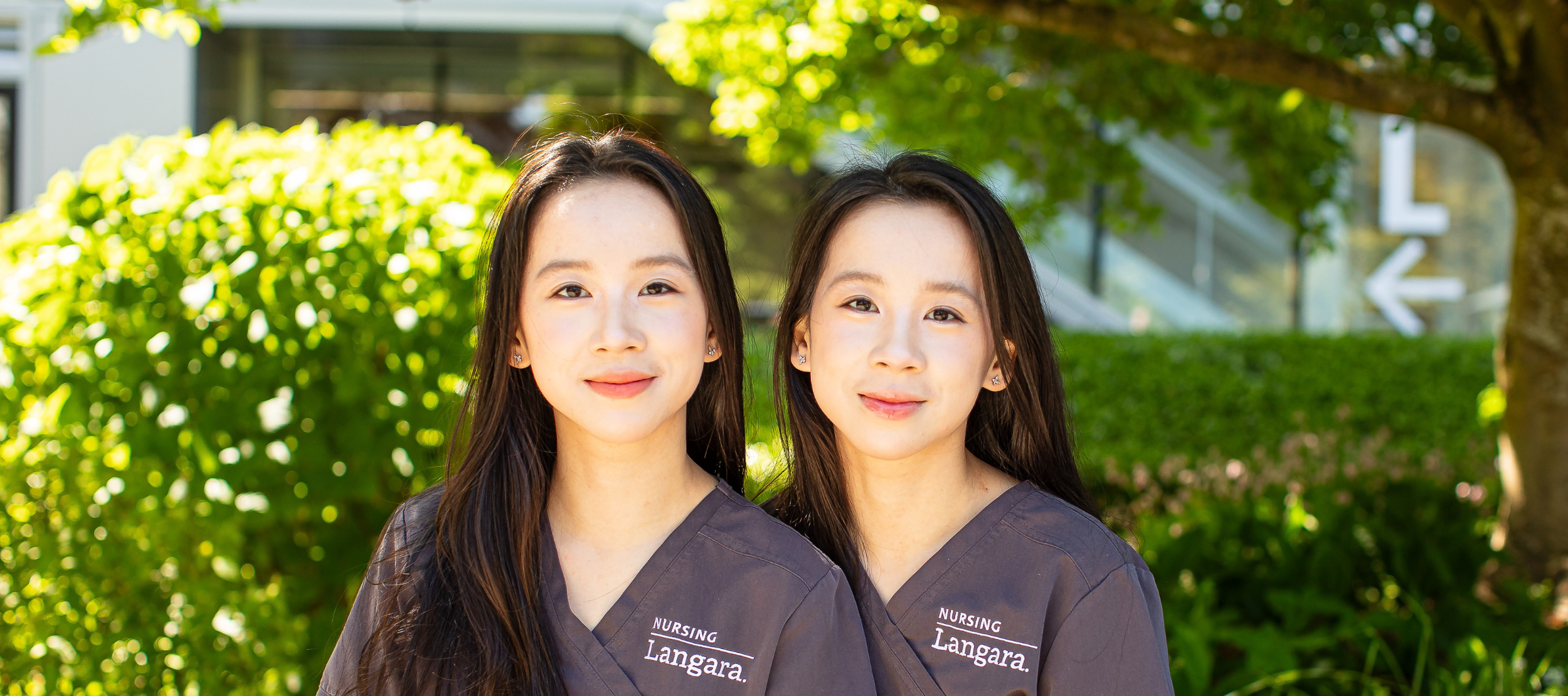 Nursing alum and sisters, Cecilia and Mandy He, sitting on a bench outside Langara's Science and Technology Building.