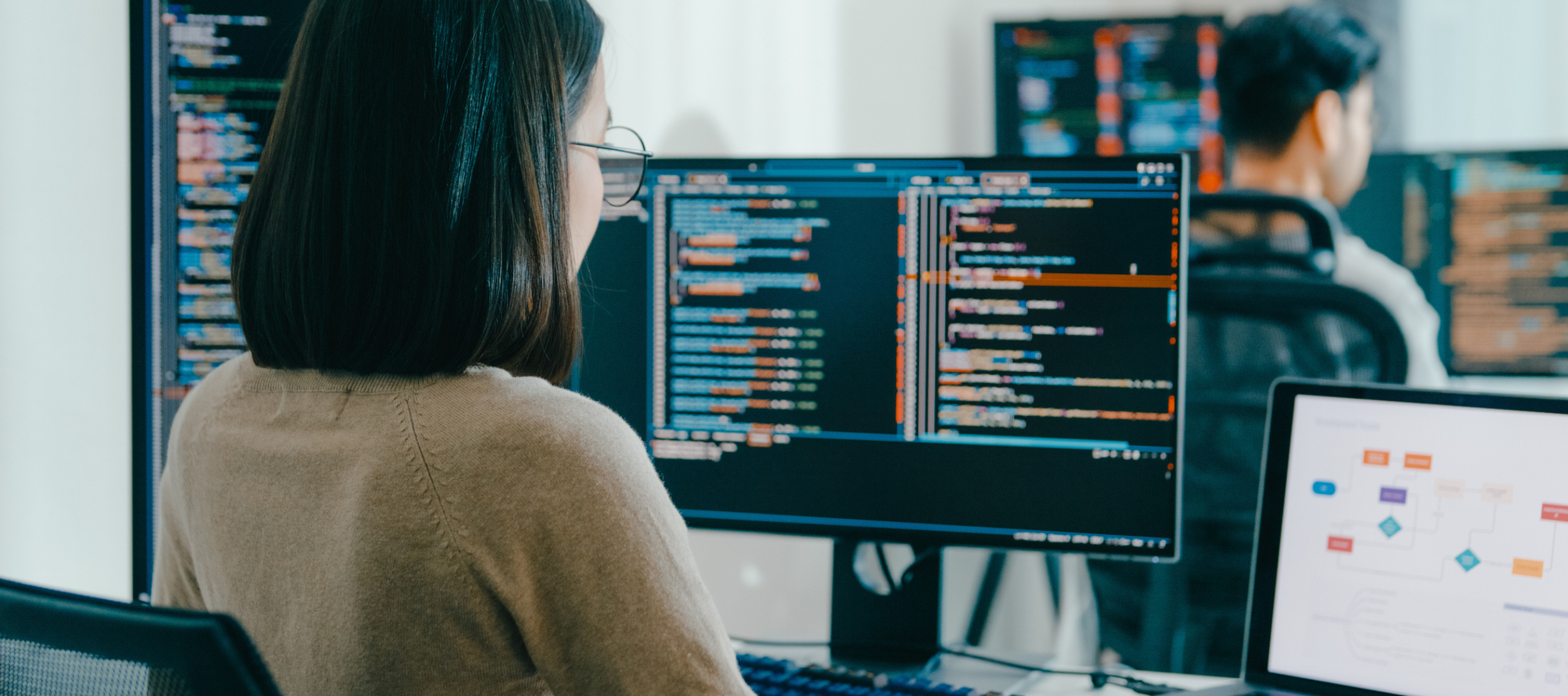 Asian woman sitting in front of a computer looking at coding and data.