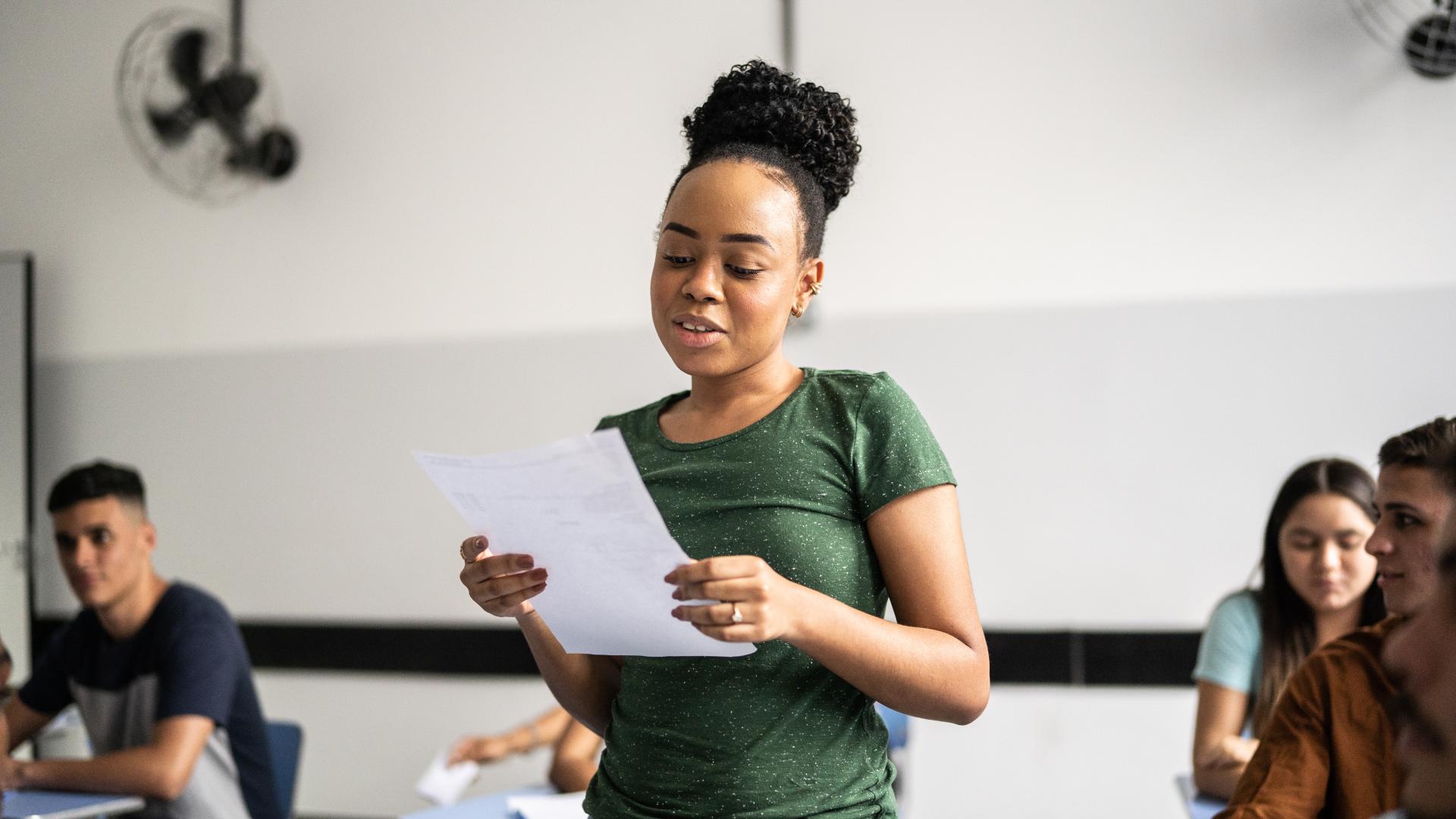A student reads in front of her class from a paper in her hands.