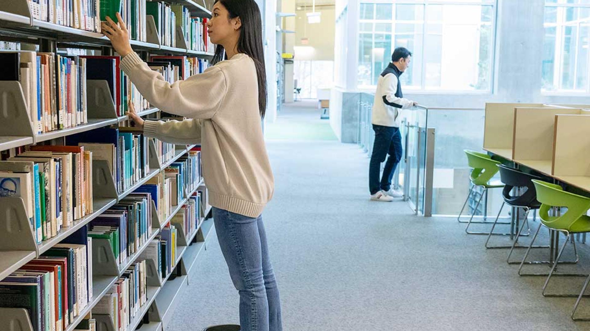 On the third floor of the library, a determined student is on a quest, her eyes scanning the shelves for the perfect book to complete her final assignment.