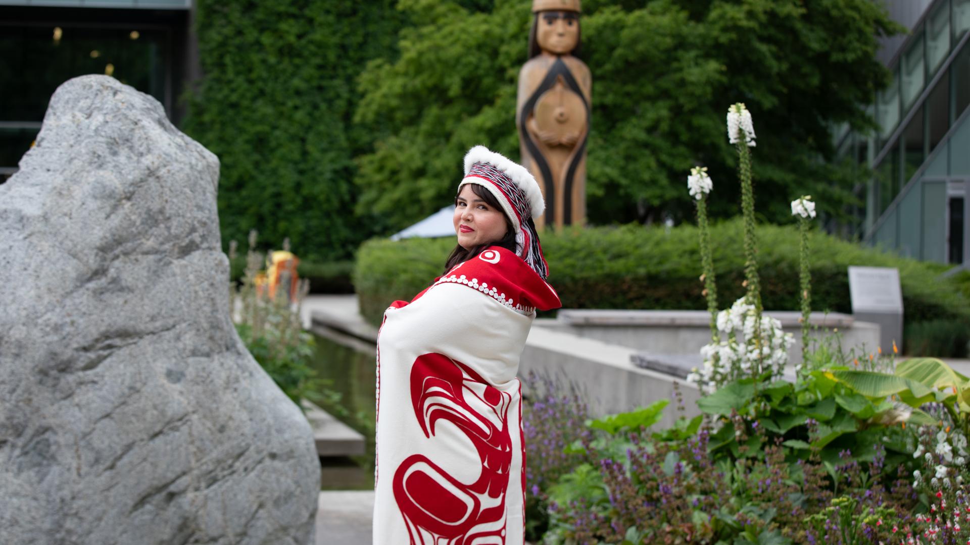 Bachelor of Science in Nursing graduate, Cecelia Simeon, wearing traditional Haida garments, posing in front of Langara College's Musqueam house post.