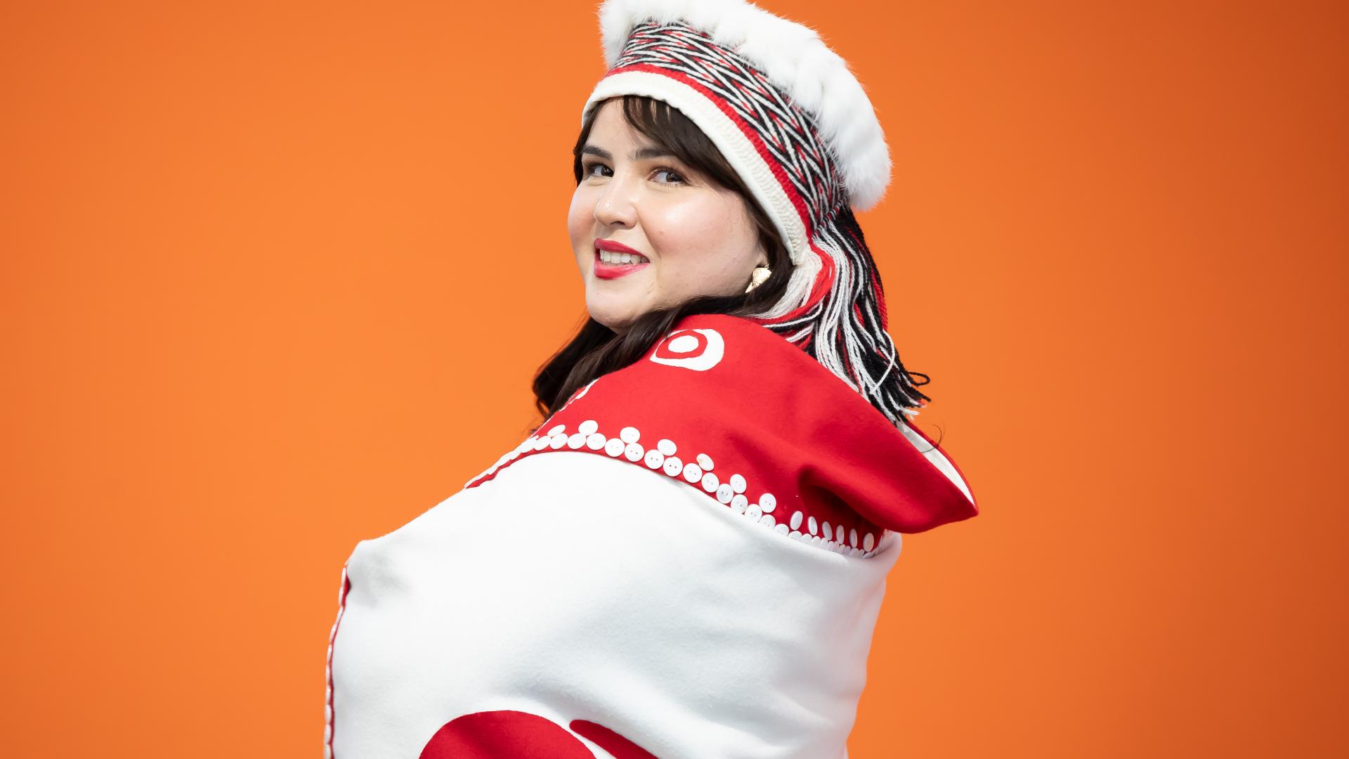 Nursing graduate, Cecelia Simeon, wearing traditional Haida garments against an orange background.