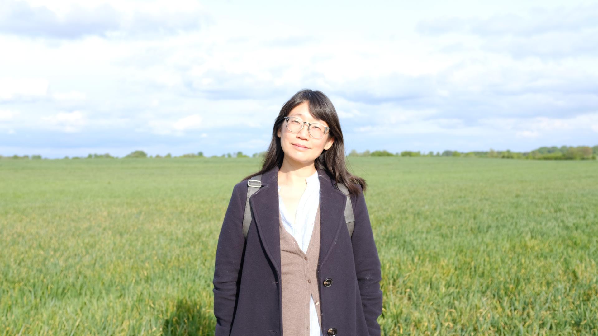 2026 Writer in Residence, Madeleine Thien, stands in a grassy field. Photo by Rawi Hage.