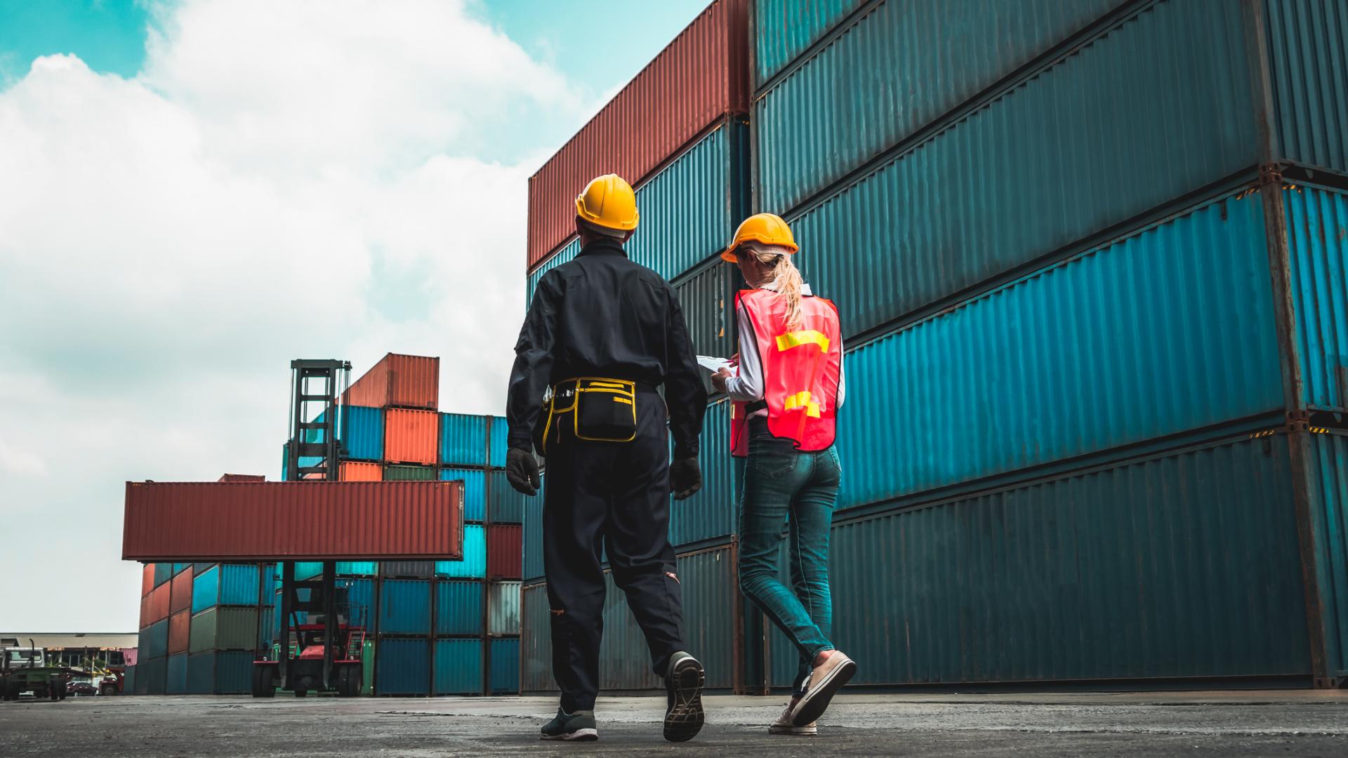 Two supply chain and logistics workers walking amongst shipping containers.