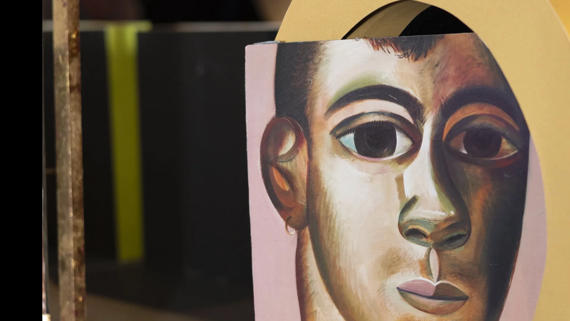 Sculptural artwork of a painted face intersecting a large gold ring on a black and gold base.