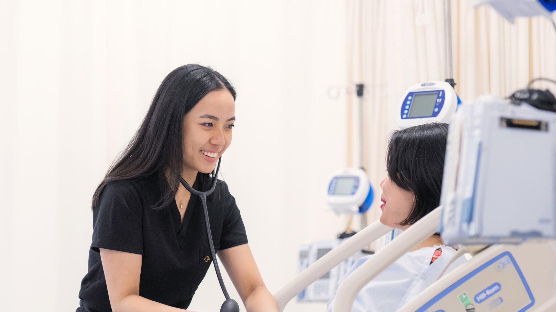 A nurse with a stethoscope providing care to a patient in a hospital bed.