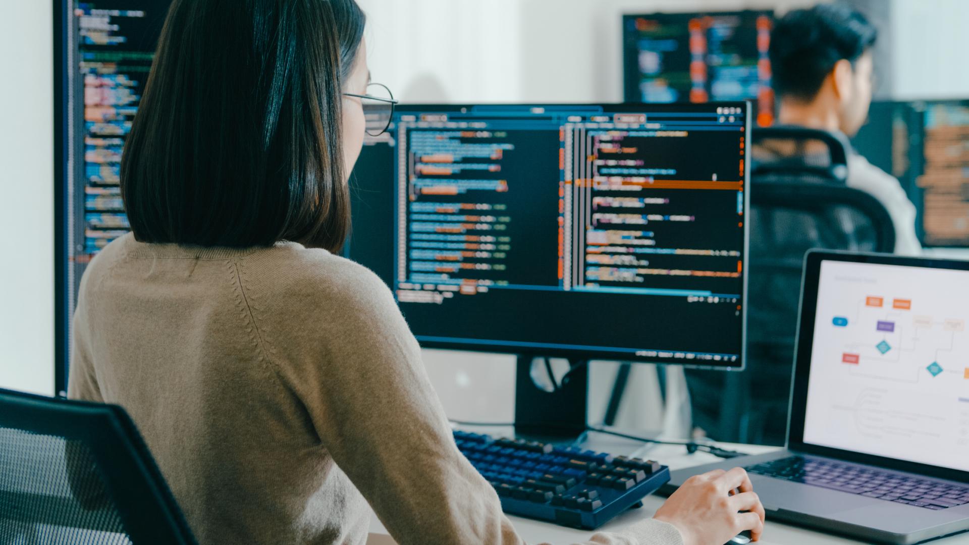 Asian woman sitting in front of a computer looking at coding and data.