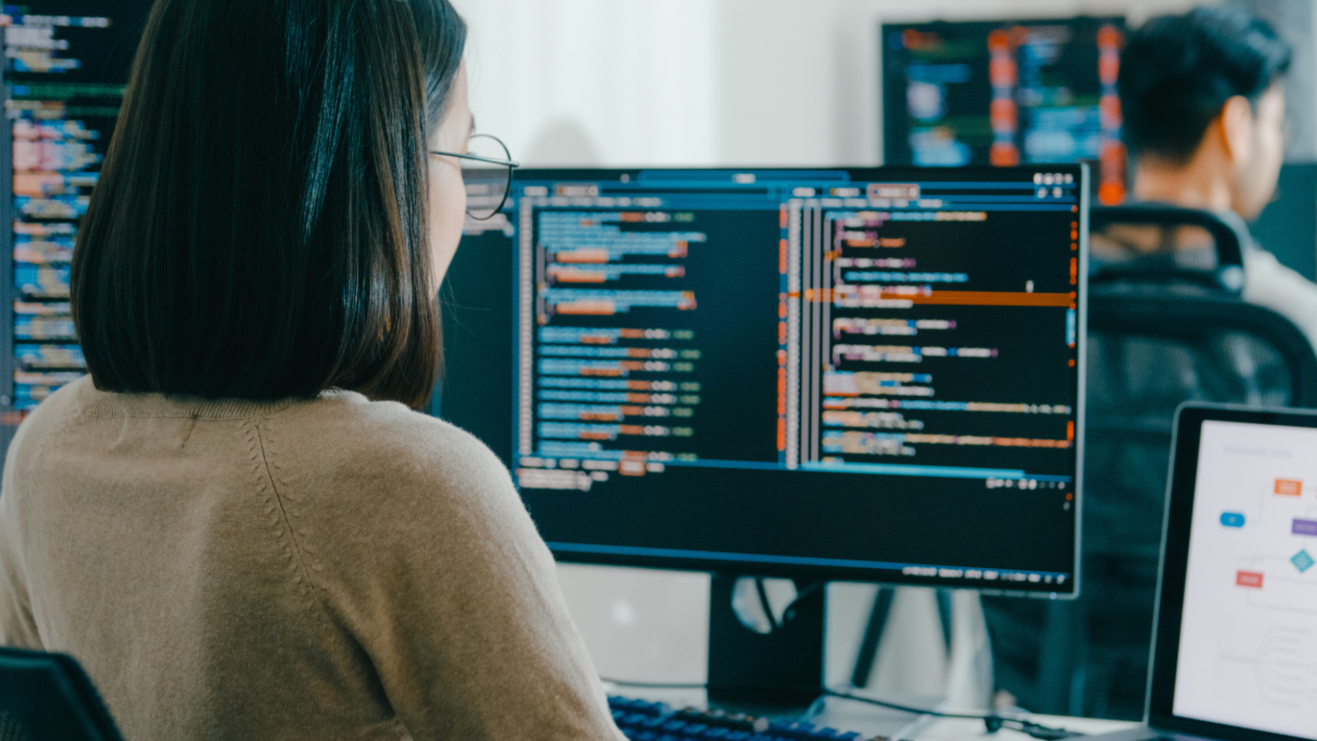 Asian woman sitting in front of a computer looking at coding and data.