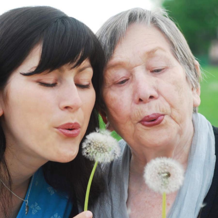 An older woman and a young woman blow wishes on dandelions.