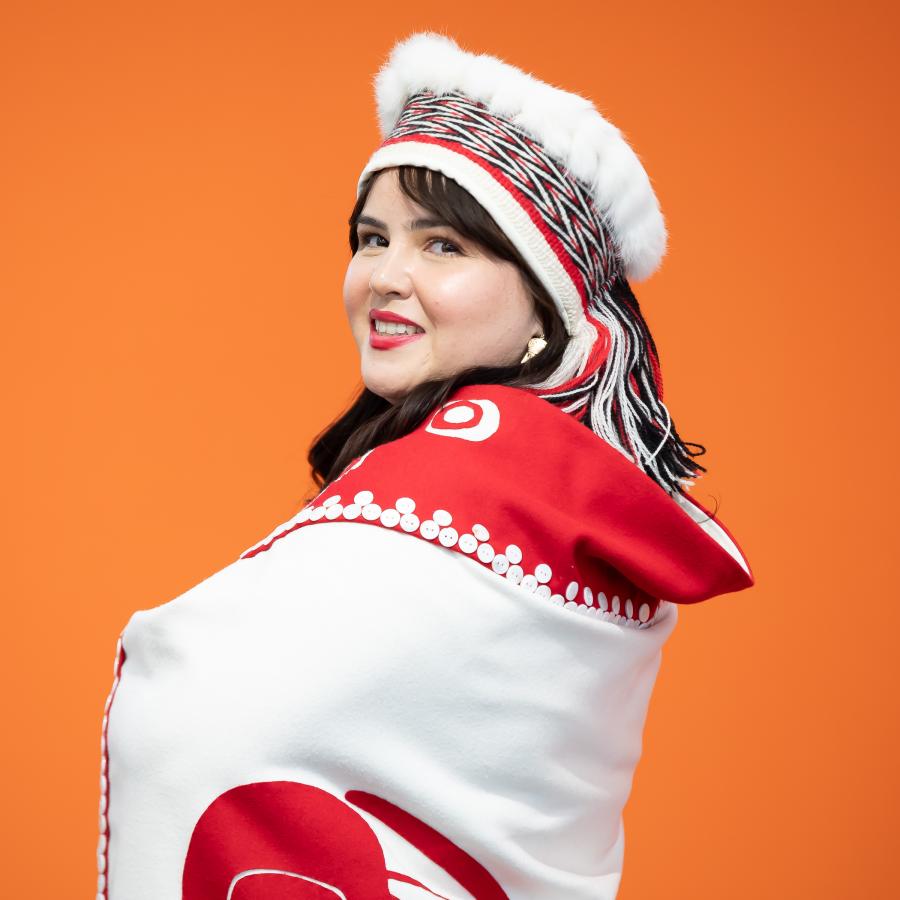 Nursing graduate, Cecelia Simeon, wearing traditional Haida garments against an orange background.