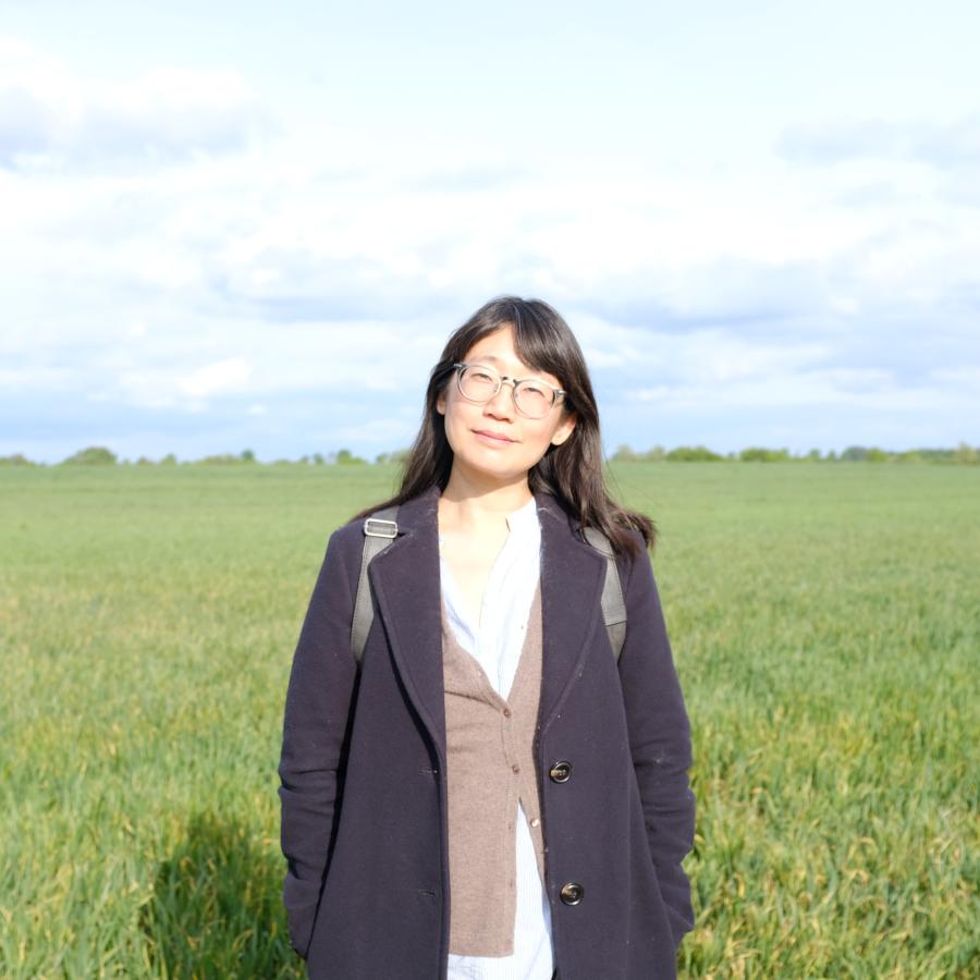 2026 Writer in Residence, Madeleine Thien, stands in a grassy field.