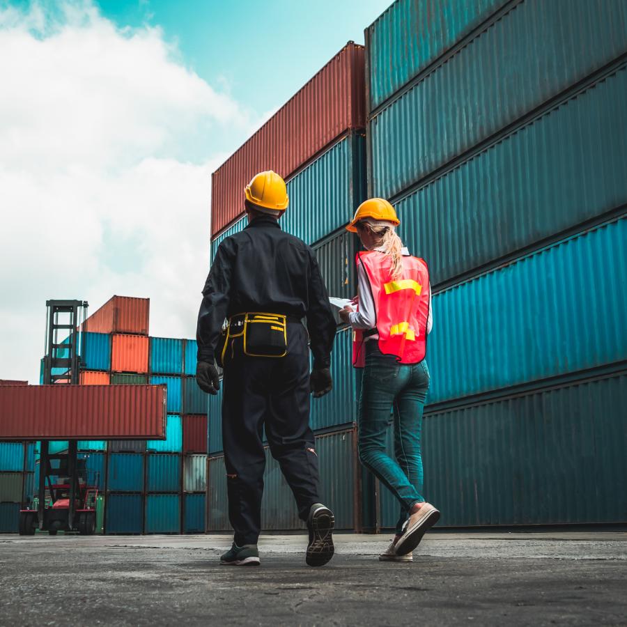 Two supply chain and logistics workers walking amongst shipping containers.