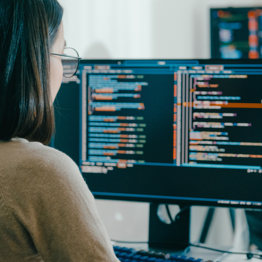 Asian woman sitting in front of a computer looking at coding and data.