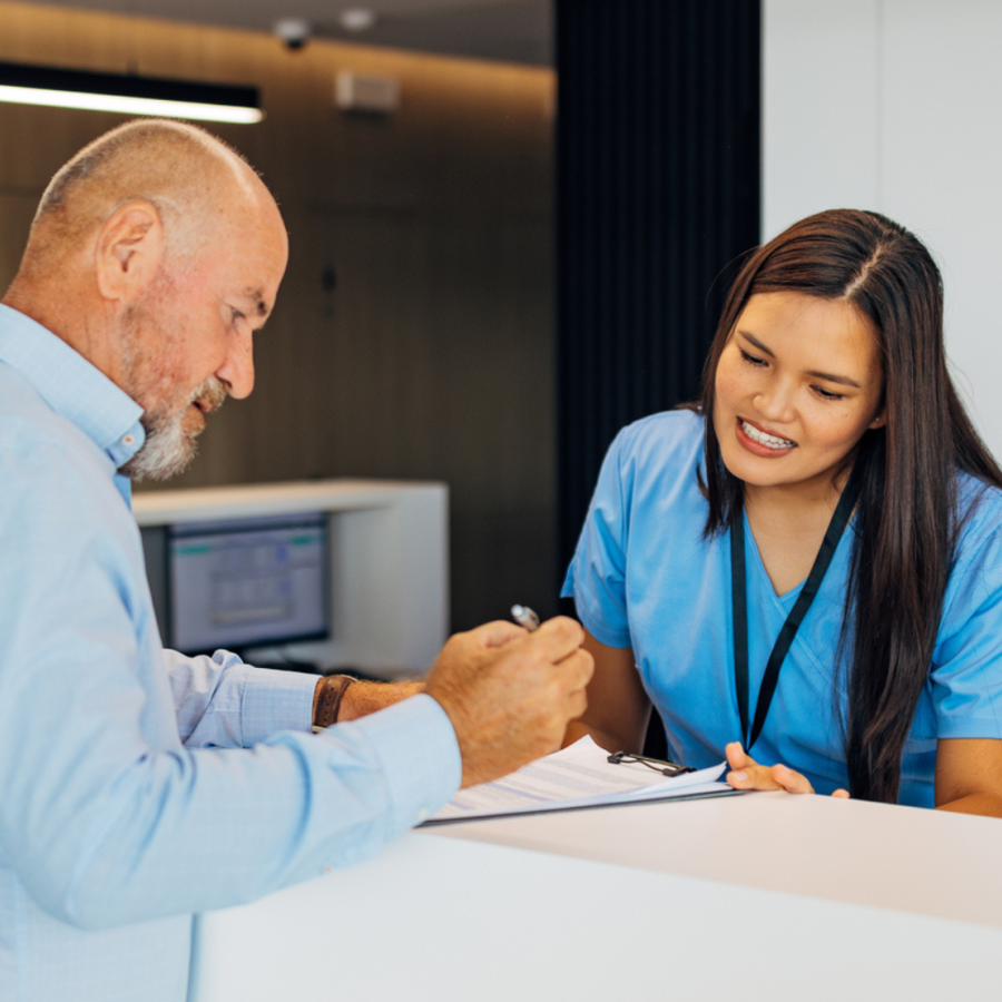 Stock image of the front desk at a medical office, with an office administrator assisting a patient.