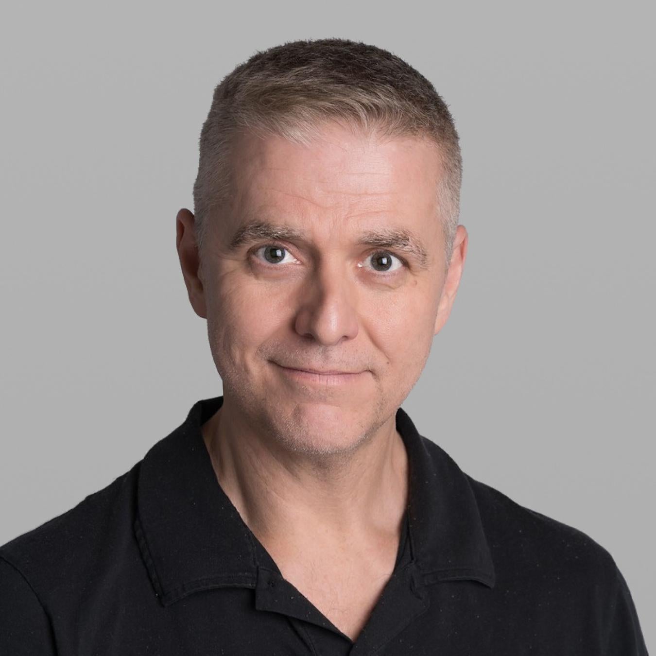 Headshot of Giuseppe Gallaccio, with short light grey hair and a black polo shirt, against a grey background.