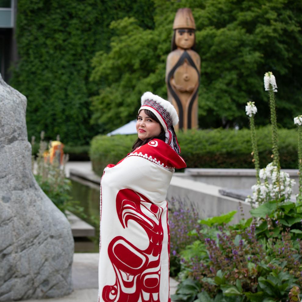 Bachelor of Science in Nursing graduate, Cecelia Simeon, wearing traditional Haida garments, posing in front of Langara College's Musqueam house post.