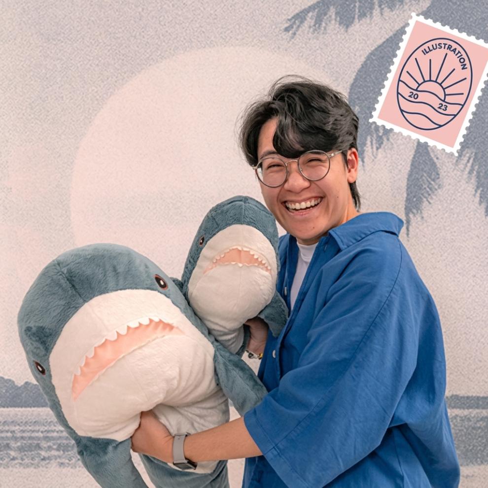 Smiling person wearing glasses and a blue shirt, holding two large plush shark toys in front of a pastel illustration-style background with a small stamp graphic that reads “Illustration 2023.”
