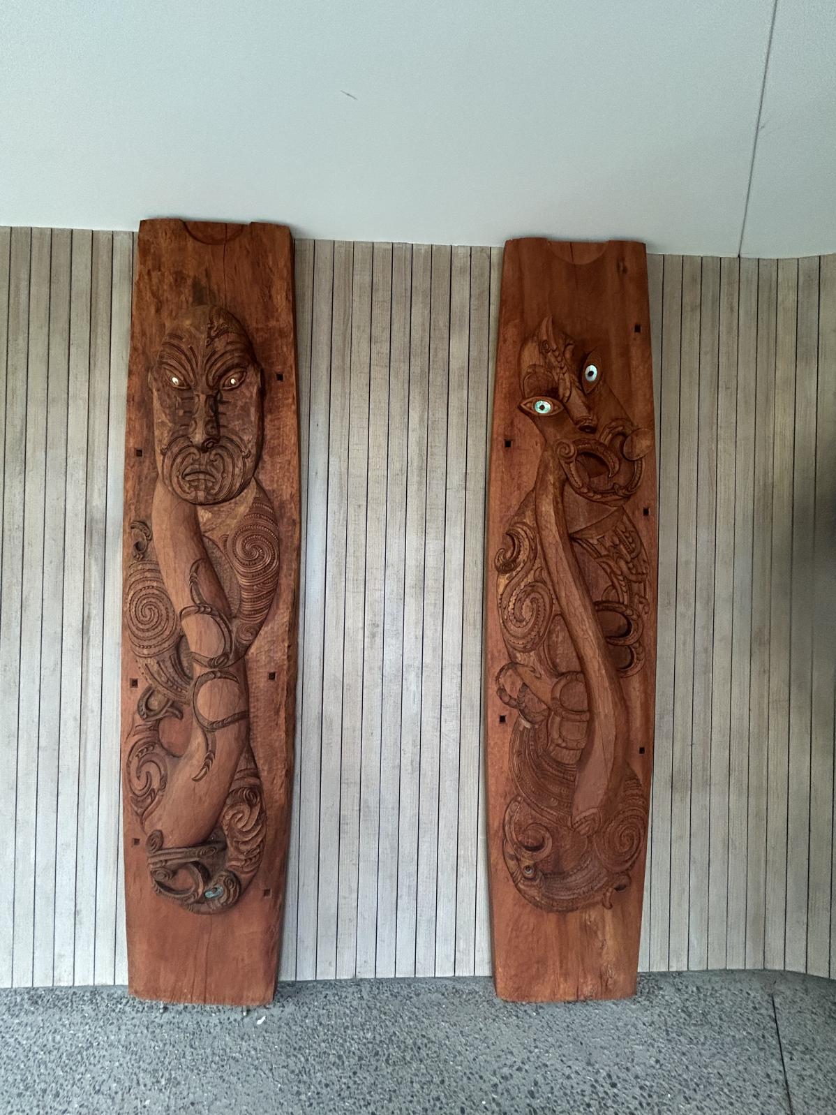 Two large Māori carvings against a wall.