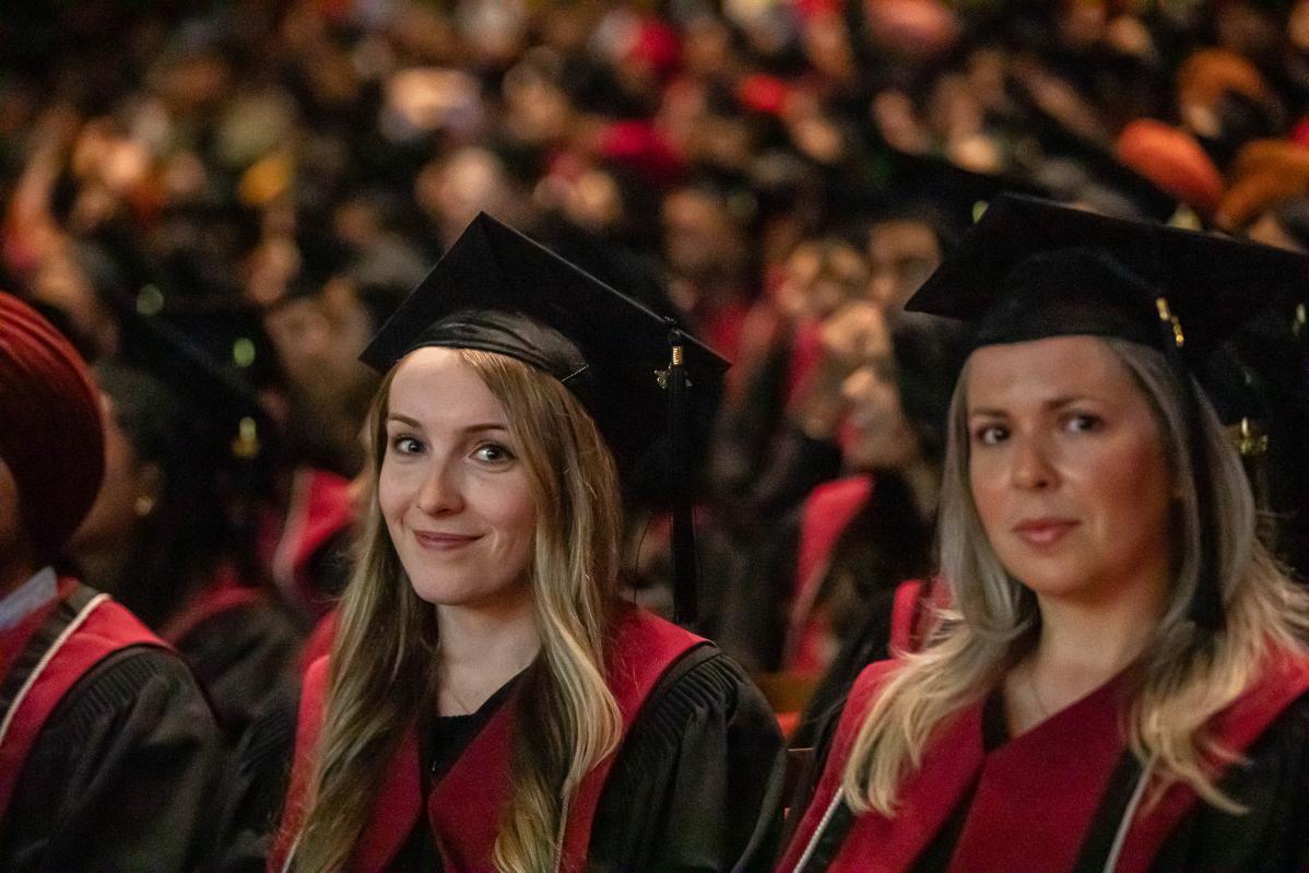 A blonde female graduating student smiles for the camera in the crowded convocation hall.