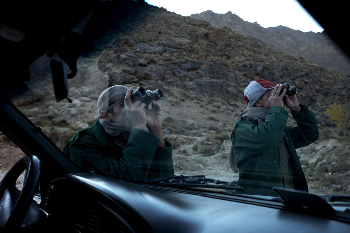 Two men look through binoculars at a far away sky. 