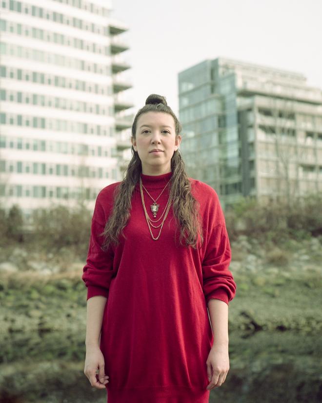 Ming Hudson: Long brown hair down each side of her head. Vibrant red dress with jewellery around her neck.