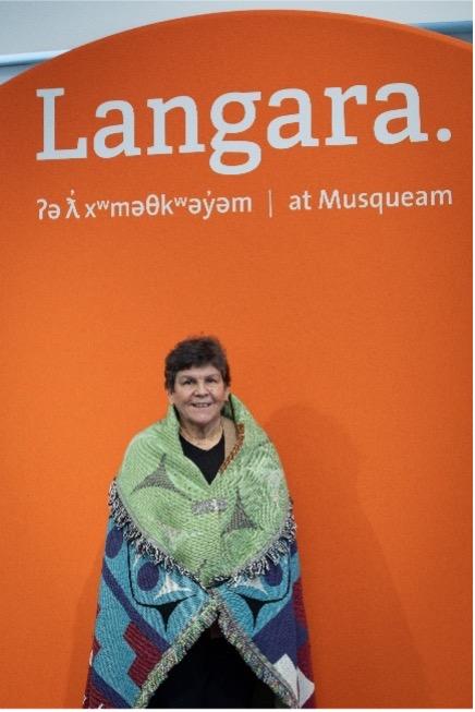 Elder Gail Sparrow smiles while wrapped in an intricate Musqueam blanket.