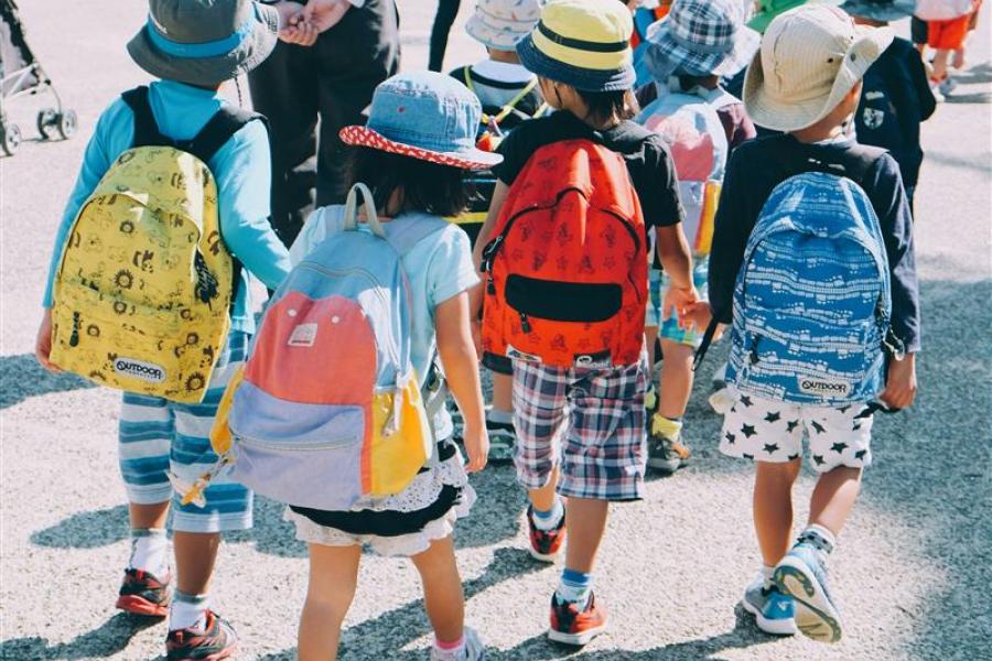 From the back, a group of children in hats take a walk in the sunshine.