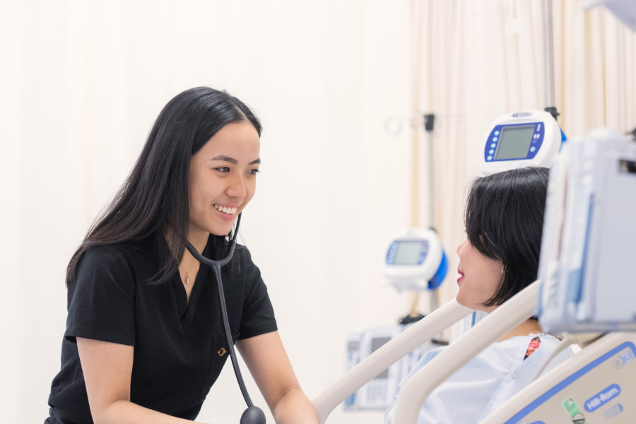 A nurse with a stethoscope providing care to a patient in a hospital bed.