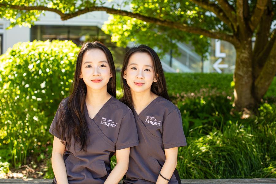 Nursing alum and sisters, Cecilia and Mandy He, sitting on a bench outside Langara's Science and Technology Building.
