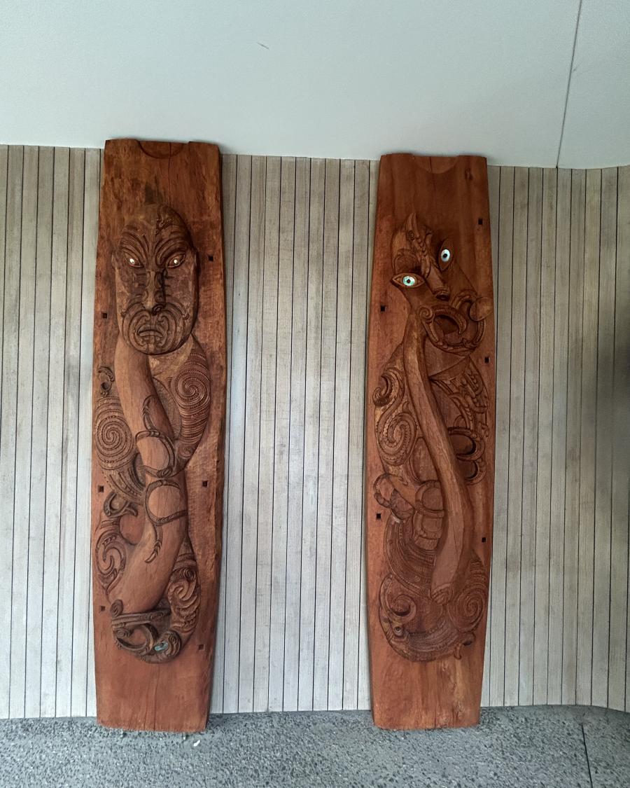 Two large Māori carvings against a wall.