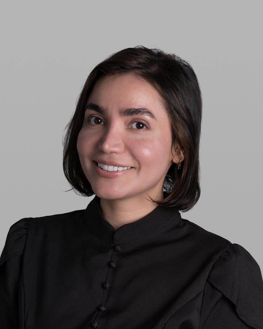 Headshot of Binazir Farokhi, smiling, with a dark chin-length bob and a black high-collared blouse, against a grey background.