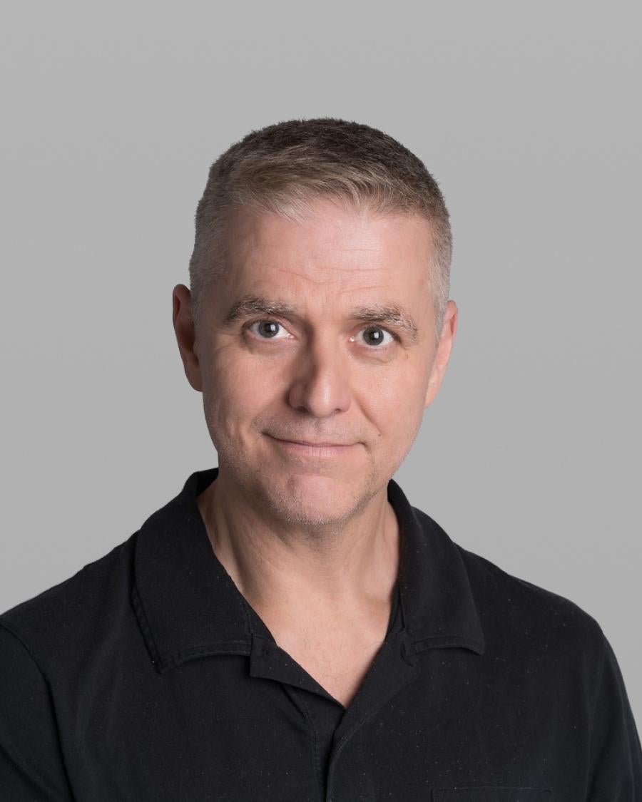 Headshot of Giuseppe Gallaccio, with short light grey hair and a black polo shirt, against a grey background.
