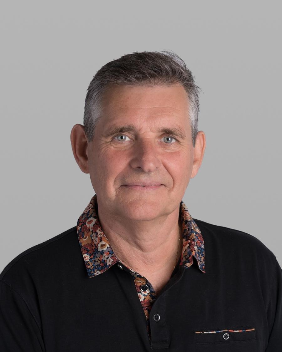 Headshot of Terry Van Roon, with short grey hair and a black jacket over a floral-patterned shirt, against a grey background.